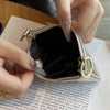 A hand holds a brown genuine leather compact coin purse and key holder with gold hardware.