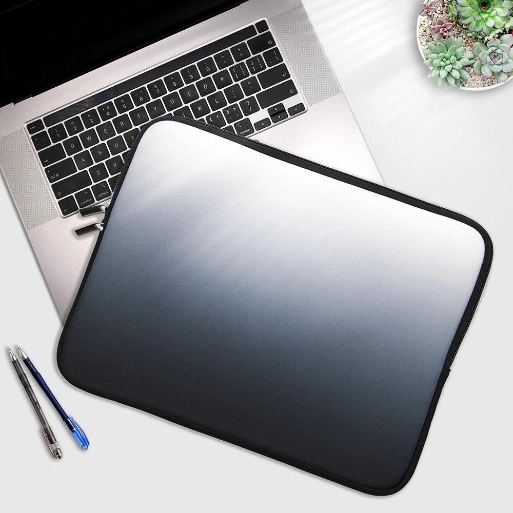 A silver laptop is shown with a black multi-size sleeve placed in front of it, next to a pen.