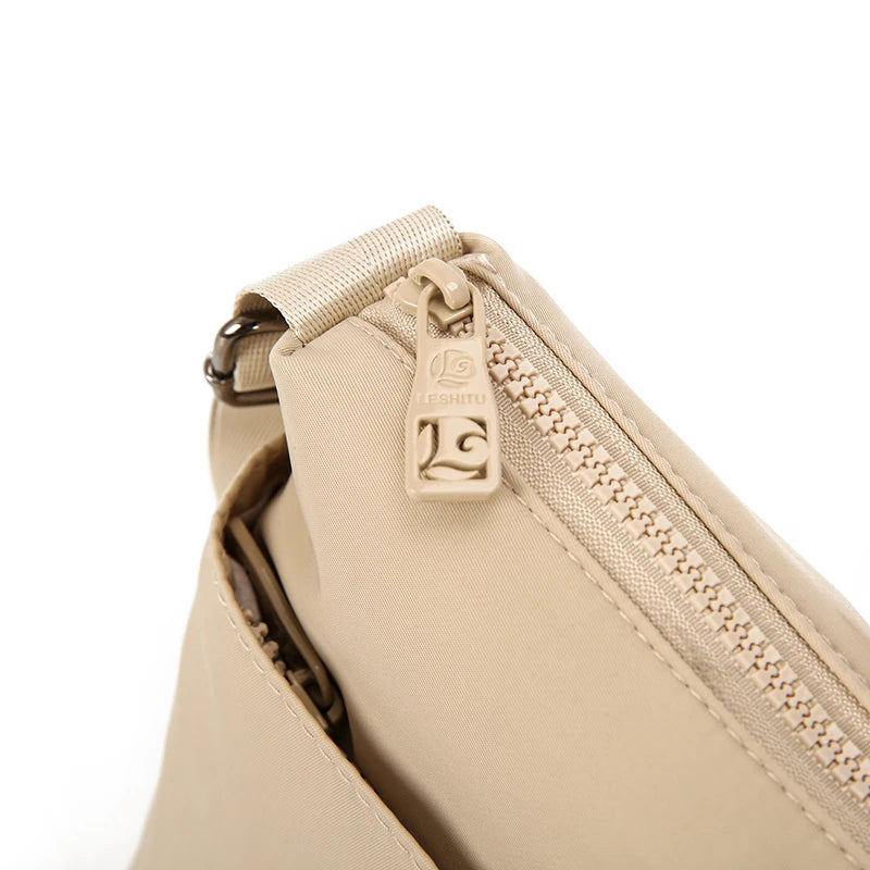 Close-up of a beige waterproof nylon crossbody bag showing the zipper and hardware.