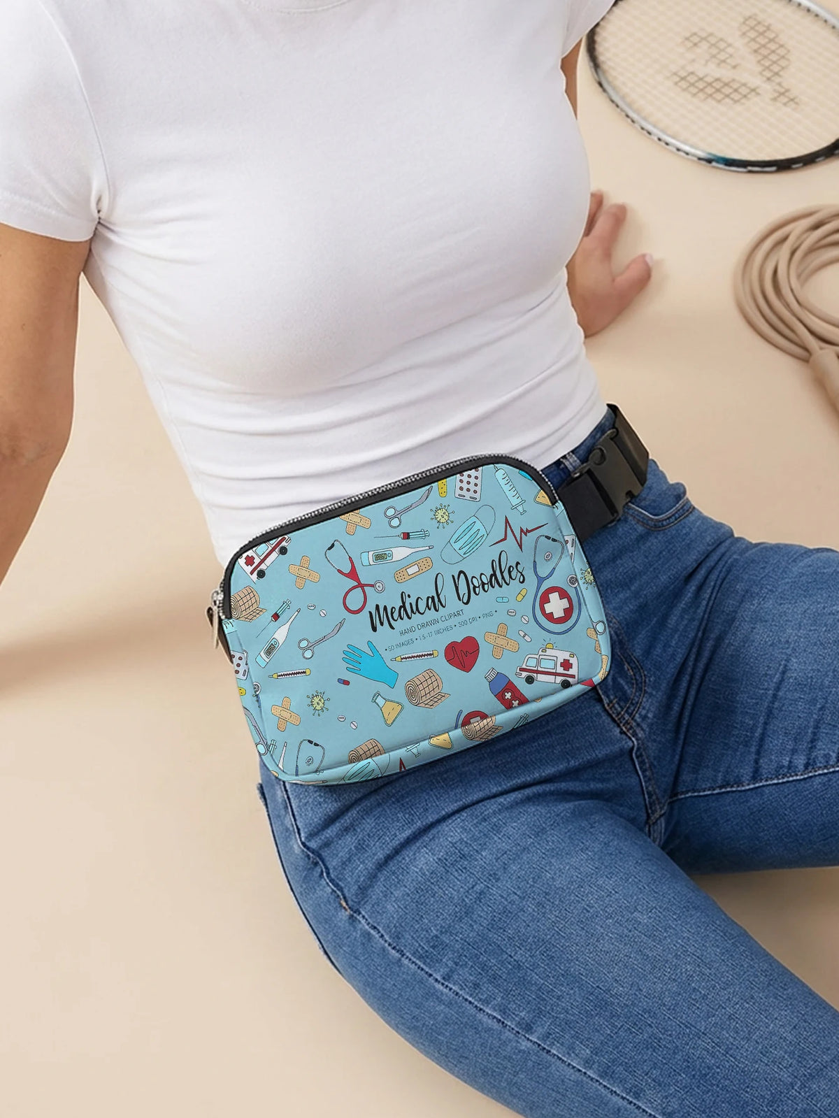 A light blue medical doodle print crossbody waist bag worn by a person in a white top and jeans.