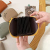 A hand holds a dark brown multi-card wallet with a yellow trim, featuring a pleated design.