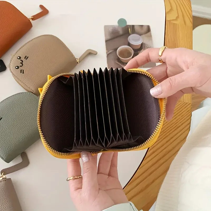 A hand holds a dark brown multi-card wallet with a yellow trim, featuring a pleated design.