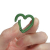 A hand holds a green heart-shaped metal spring clasp for DIY jewelry or keychains.