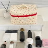 A cream-colored quilted makeup bag with a red stripe and a lid featuring a cute cartoon animal design.