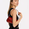 A woman holds a red PU leather shoulder bag with an adjustable strap against a white background.