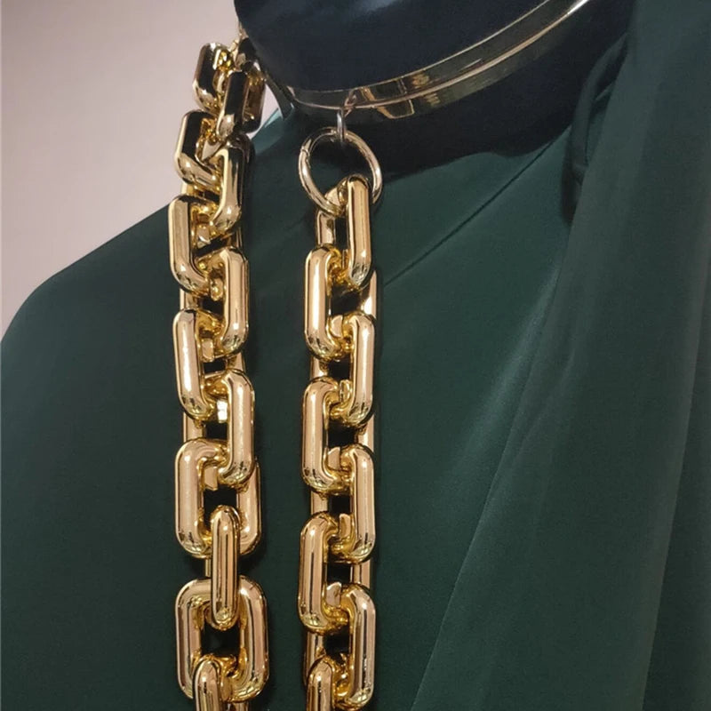 Cartera de acrílico dorado con cadena colgando de un collar de plata sobre tela verde oscura.