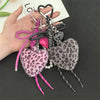 A hand holds a leopard print plush love pendant keychain with pink and black accents.
