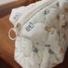 A quilted white cosmetic storage pouch with a zipper and small printed cats resting on a wooden surface.