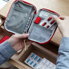 A hand opens a red compact survival kit, revealing compartments for various first aid supplies.