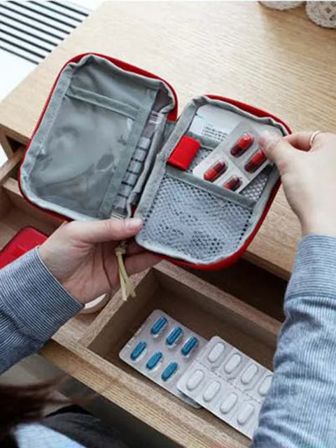 A hand opens a red compact survival kit, revealing compartments for various first aid supplies.