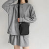 Une personne portant un sweat-shirt et une jupe grises tient un sac bandoulière noir.