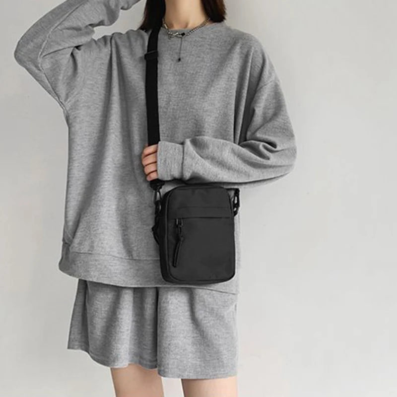 Une personne portant un sweat-shirt et une jupe grises tient un sac bandoulière noir.