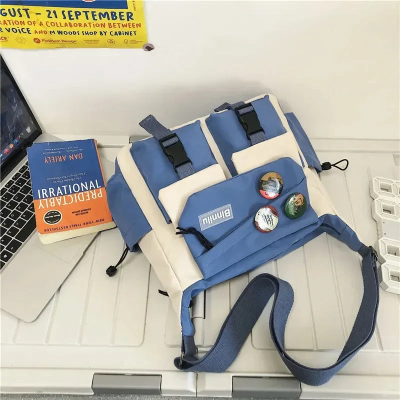A blue and beige nylon crossbody shoulder bag lying on a white desk next to a laptop.