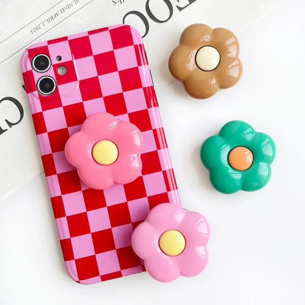 Coque de téléphone à carreaux rose et rouge avec trois grips en forme de fleur dans des tons de rose, jaune et marron.