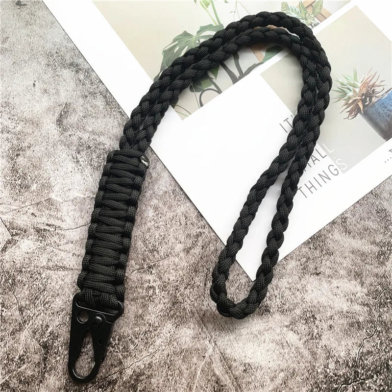 Black hand-woven nylon lanyard with a metal hook lying on a gray textured surface.