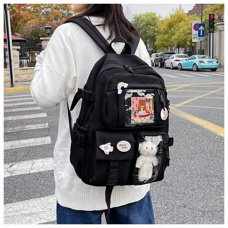 A woman wearing a white sweater carries a black large capacity backpack with various pockets and compartments on a city stree