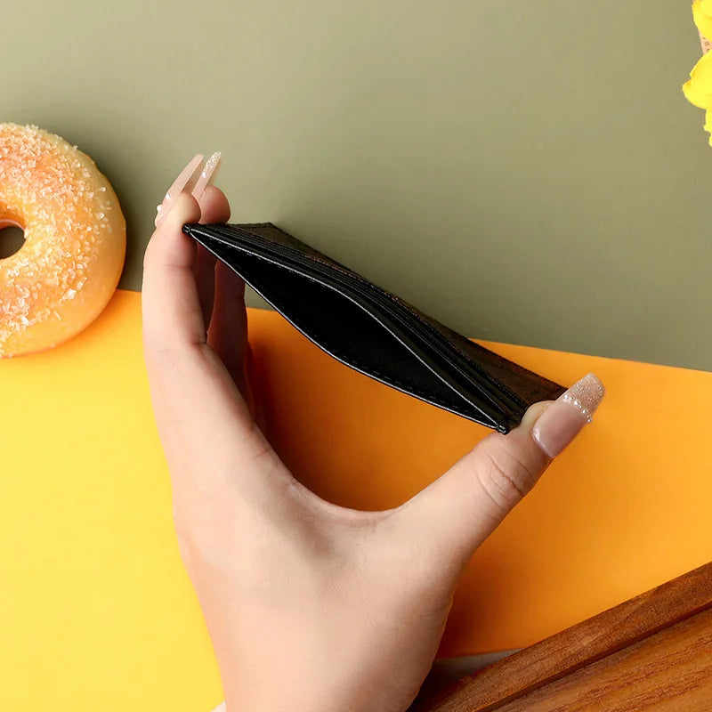 A hand holds a black elegant PU leather card holder purse against a bright orange background.