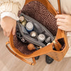 A close-up of a brown leather handbag showing an interior organizer with various small bottles and accessories.