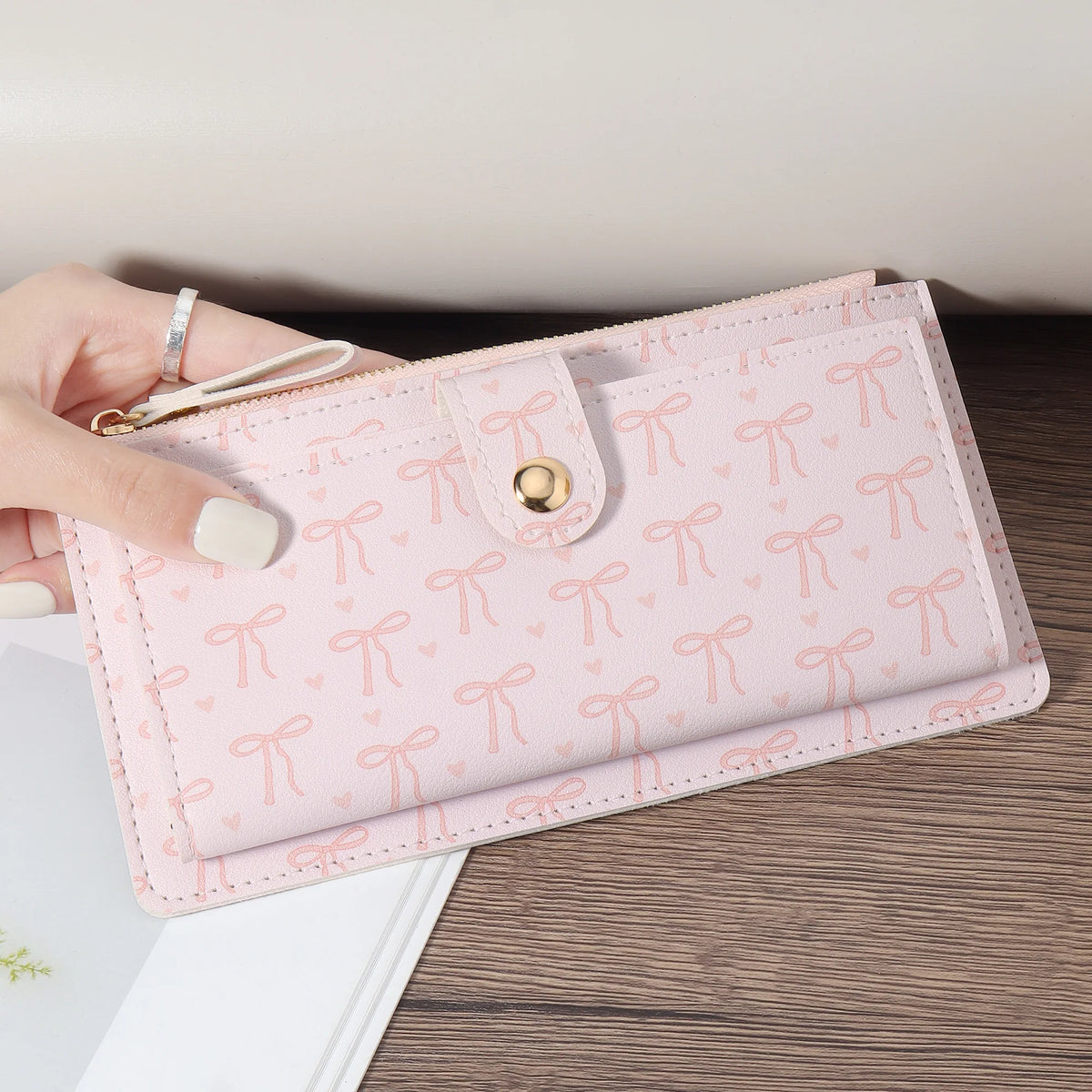 A pink elegant folding multi-card wallet is held by a hand on a wooden surface.