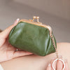 A hand holds a olive green leather coin purse with a gold chain keychain against a neutral background.