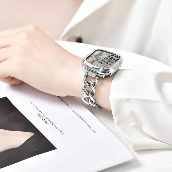 A close-up of a silver stainless steel watch strap with a square watch face worn on a wrist next to a white shirt and a noteb