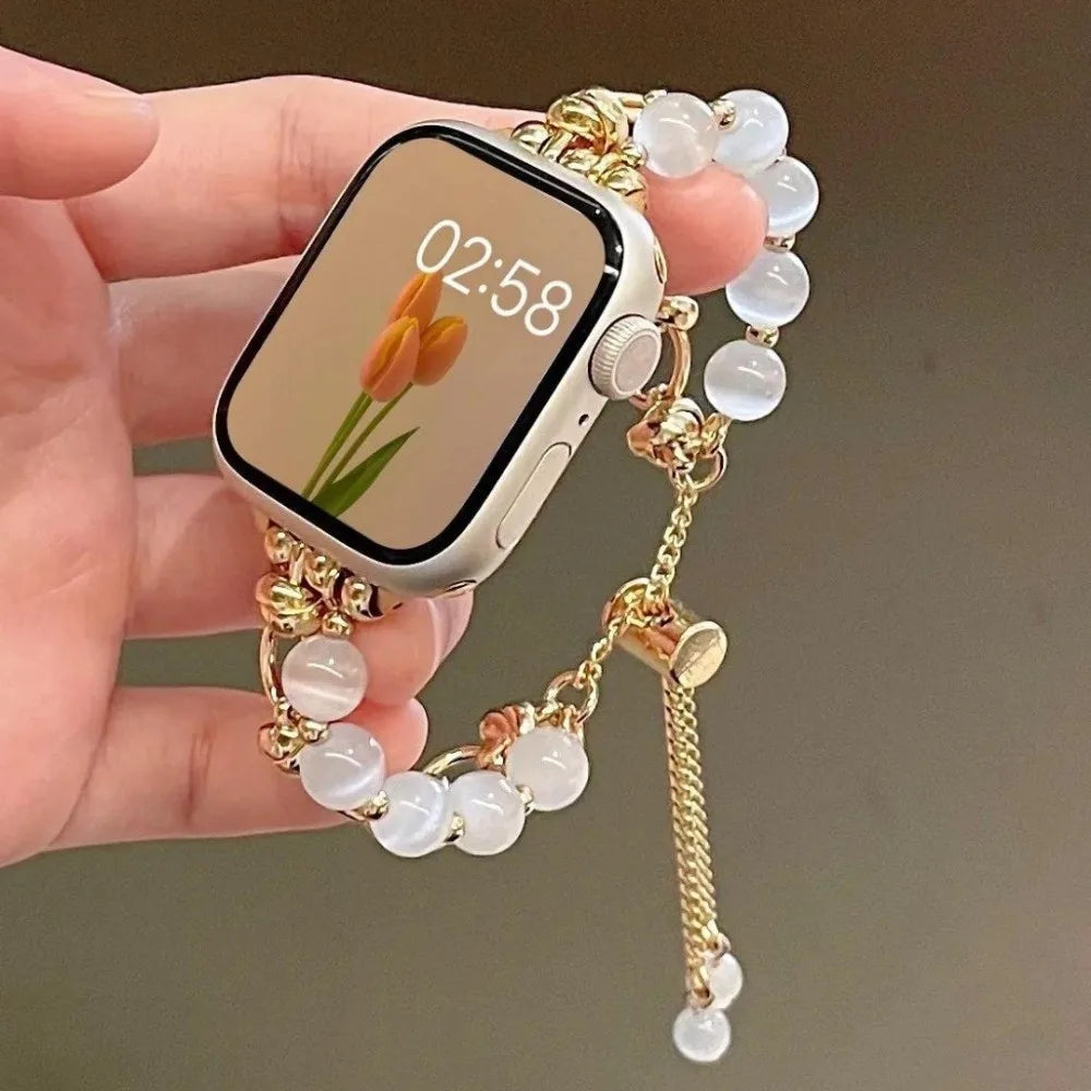 Eine Hand hält ein verstellbares Metallarmband mit klaren Kristallperlen und eine Smartwatch, die 02:58 anzeigt.