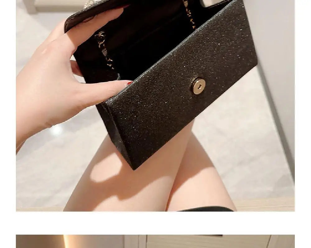 Una mano sostiene un bolso de mano negro con lazo brillante y herrajes dorados.