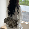 A woman stands by a window holding a leopard print riveted shoulder bag.