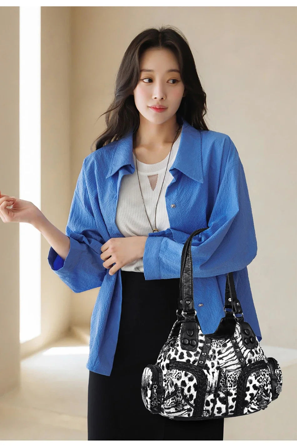 A woman models a blue denim shirt and black pants while holding a black and white patterned PU leather tote bag.