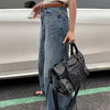 A woman wearing a white top and jeans stands next to a silver car, holding a black saddle-shaped PU leather city tote bag.