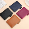 A collection of genuine leather mini zipper coin and card purses in navy blue, black, and magenta resting on a light backgrou