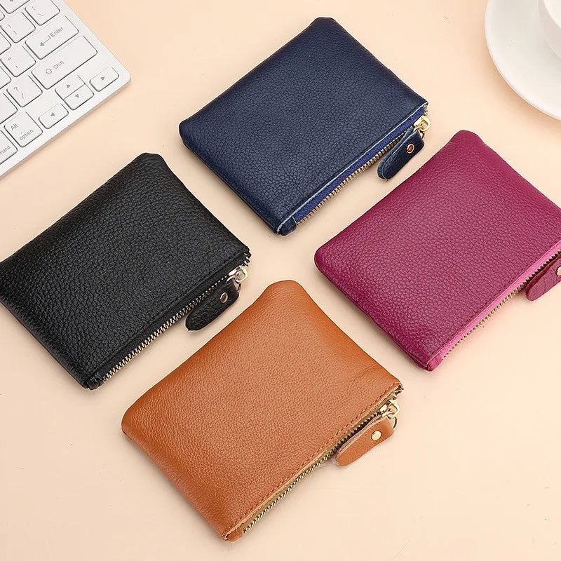 A collection of genuine leather mini zipper coin and card purses in navy blue, black, and magenta resting on a light backgrou