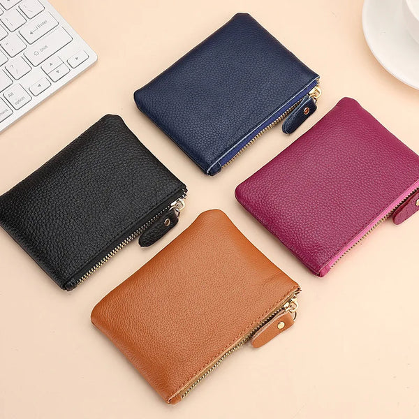 A collection of genuine leather mini zipper coin and card purses in navy blue, black, and magenta resting on a light backgrou