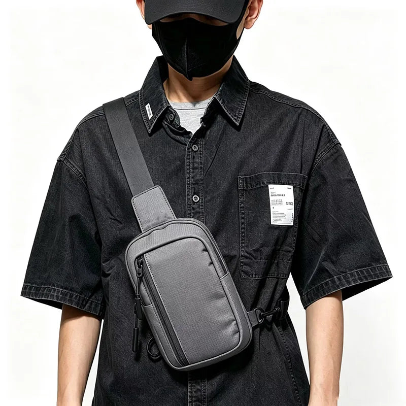 A person wearing a black shirt and face mask is holding a gray chest bag.