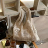 A cream-colored knitted shoulder bag displayed on a wooden surface with glass and food items.
