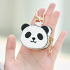 Una mano sostiene un llavero de cartera con forma de moneda de panda blanco y negro y hebilla dorada.