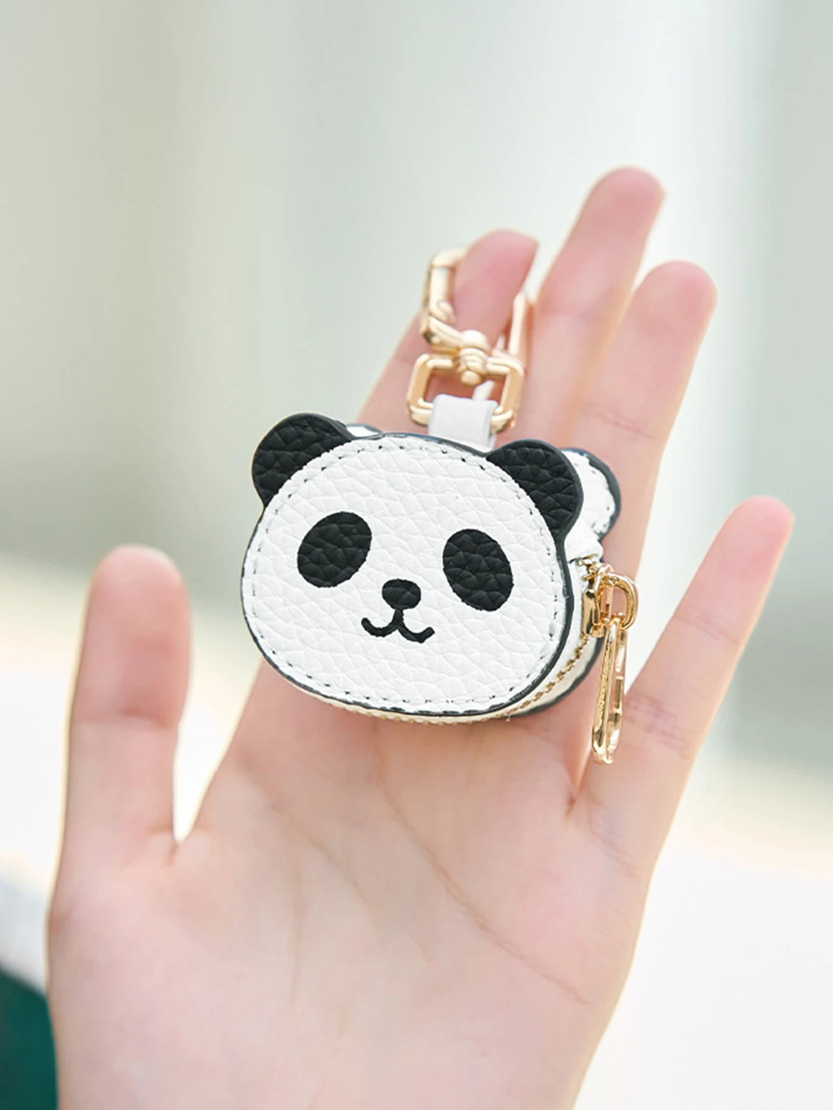 Una mano sostiene un llavero de cartera con forma de moneda de panda blanco y negro y hebilla dorada.