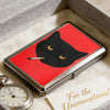 A black cat silhouette is featured on a red metal card holder resting on a white textured surface.