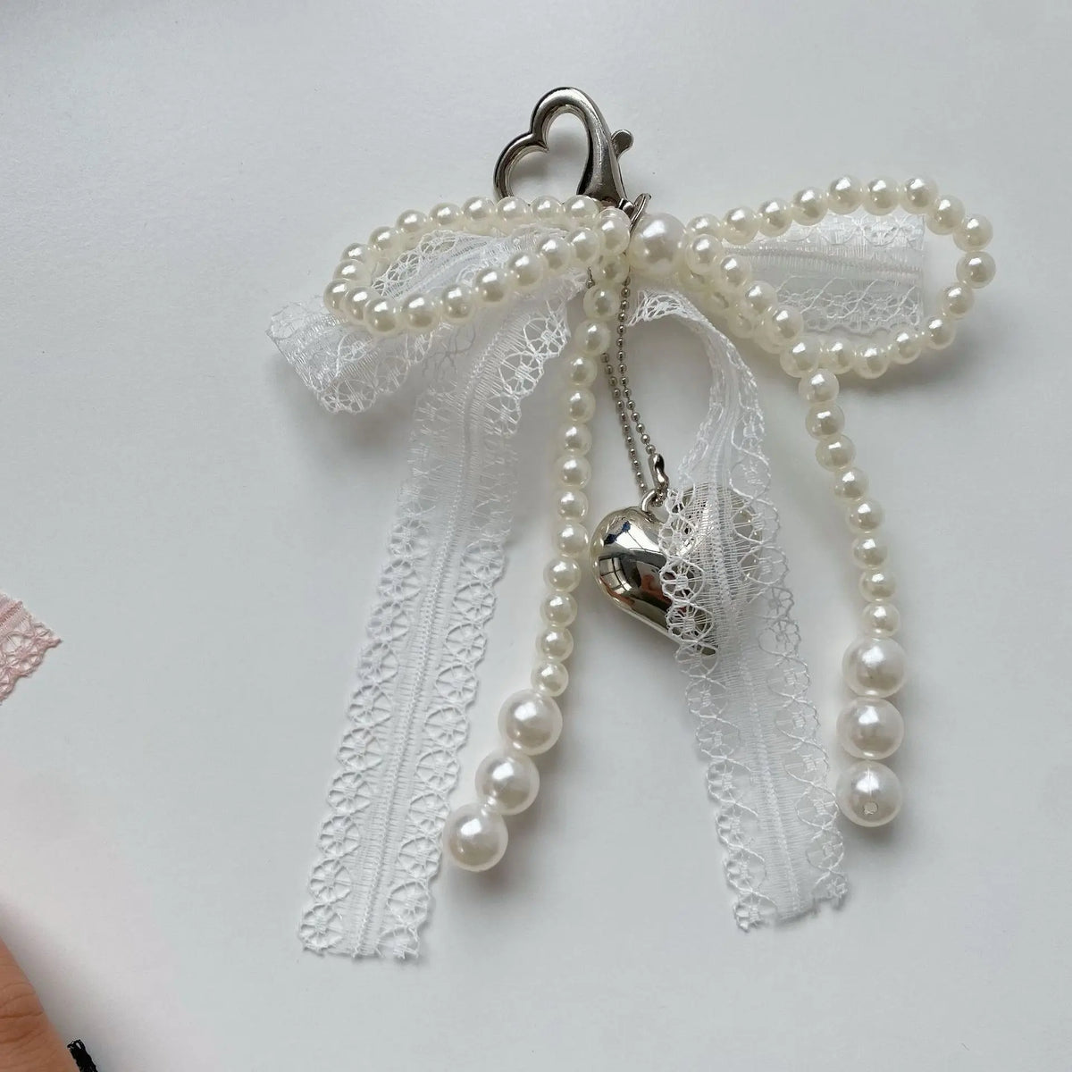 A white pearl bowknot keychain featuring a heart charm and delicate lace details.