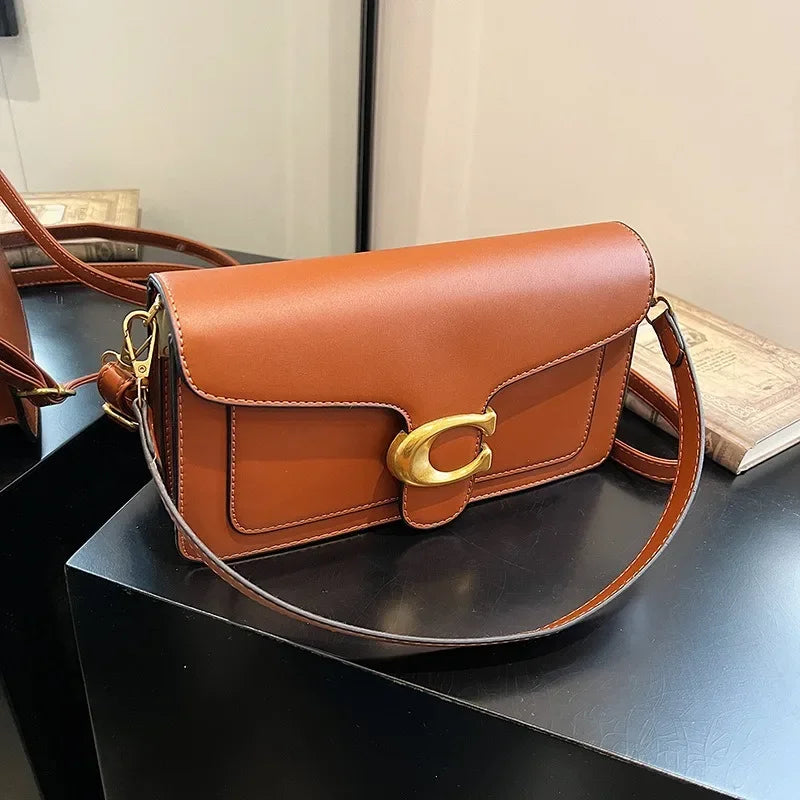 A brown leather shoulder bag with gold hardware resting on a black surface.