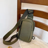 Olive green chest bag with a dark strap resting on a wooden chair.