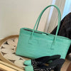 A mint green crocodile print leather handbag resting on a wooden surface.
