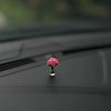 Eine kleine rosa Rosenblume in einer Glasvase auf einer dunklen Auto-Innenausstattung.