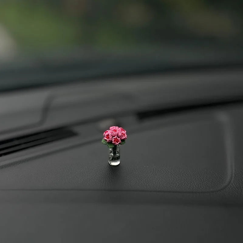 Eine kleine rosa Rosenblume in einer Glasvase auf einer dunklen Auto-Innenausstattung.