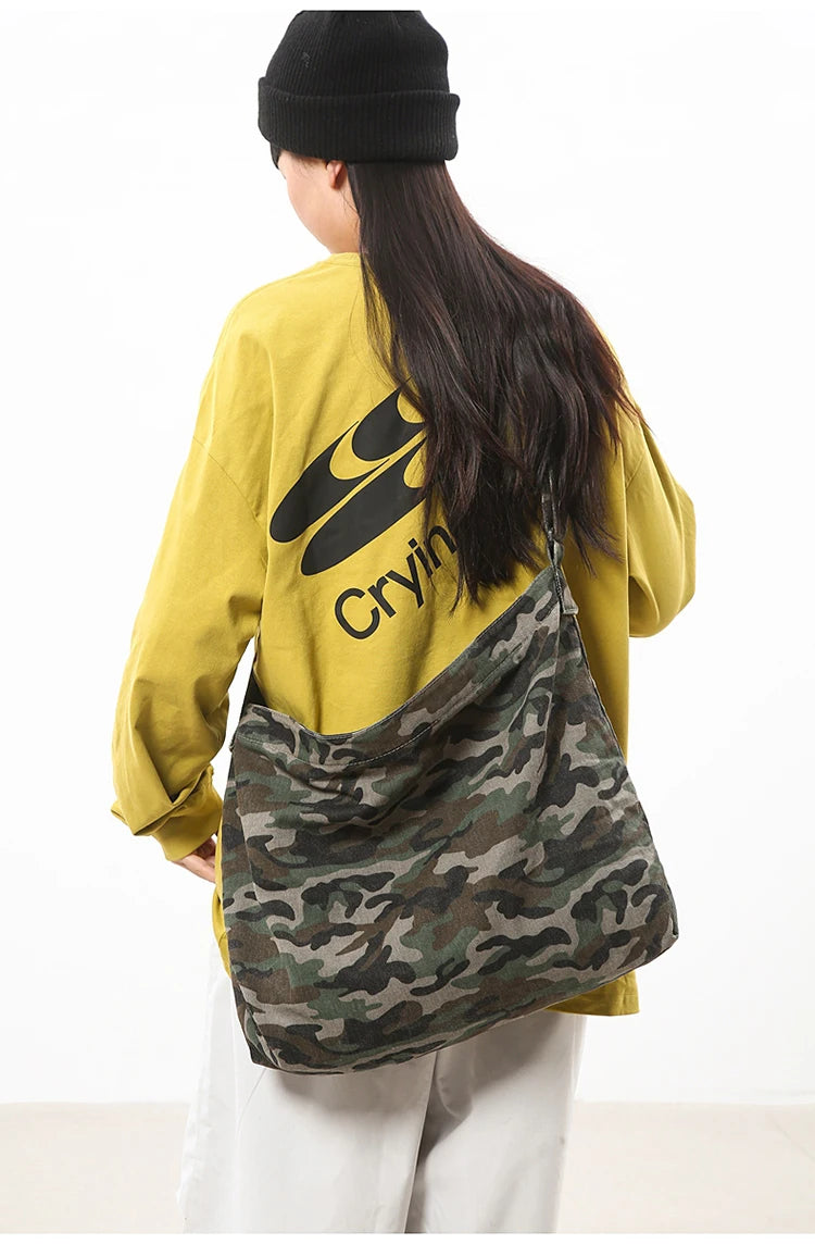 A person wearing a yellow sweatshirt and black beanie is holding a canvas camouflage shoulder bag.