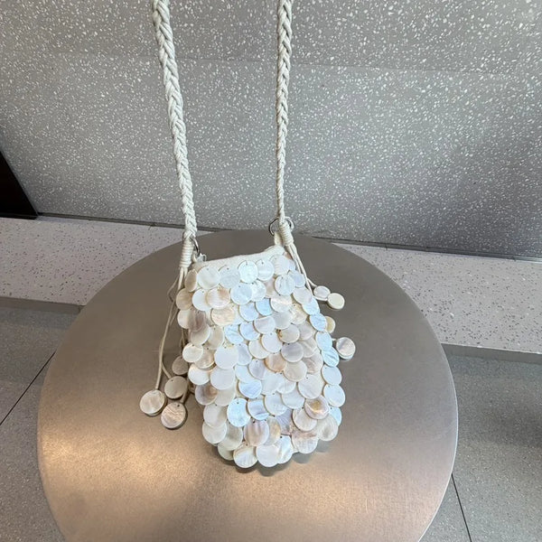 A white sequin chain shoulder bag hanging from a rope against a speckled gray background.