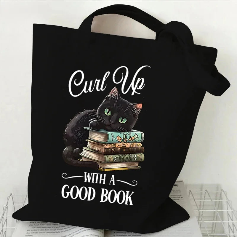 Black canvas tote bag featuring a black cat sitting on a stack of books with an orange butterfly print.