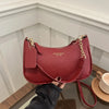 A maroon leather shoulder bag with a gold chain pendant resting on a wooden surface.