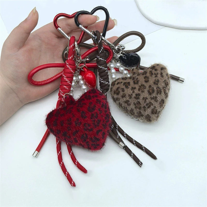 A hand holds a leopard print faux fur charm keychain with red and black leather cords and beads.