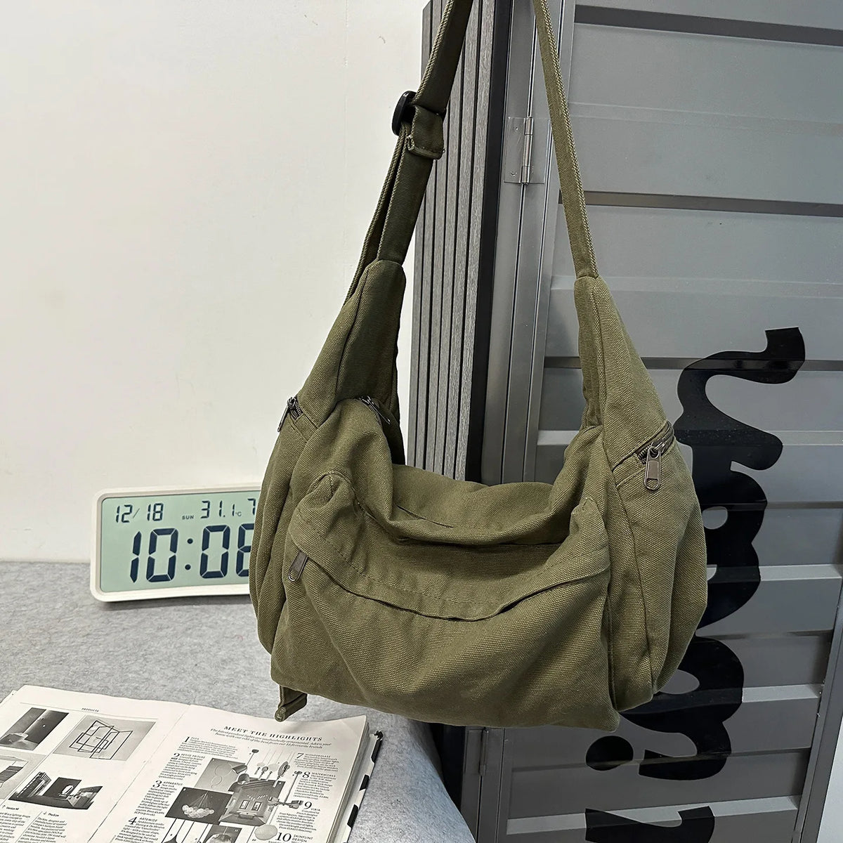 A olive green cotton canvas shoulder crossbody bag hanging on a metal grid.